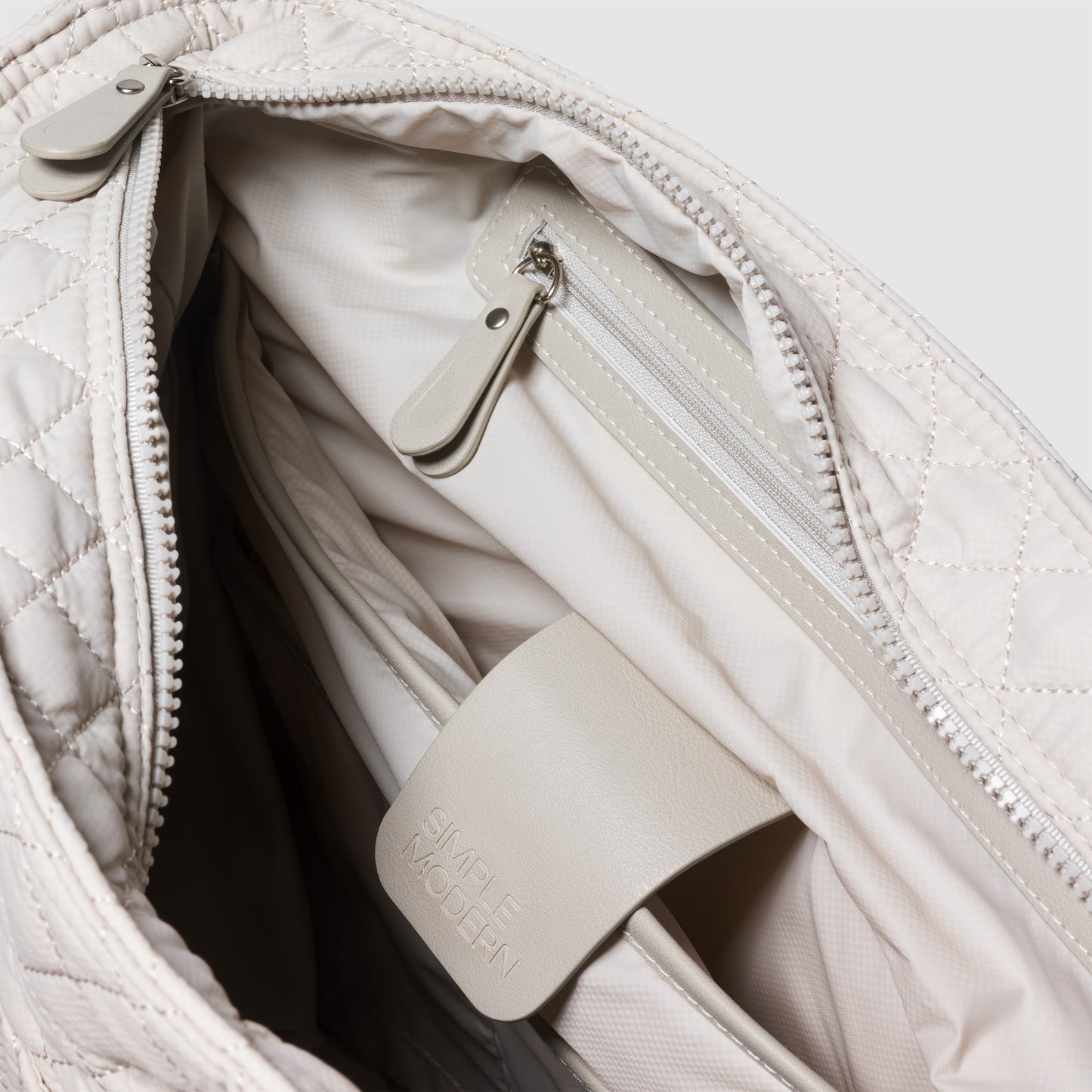 Cream and beige quilted handbag with soft gray interior, silver hardware, and structured top handle design displayed against white background.