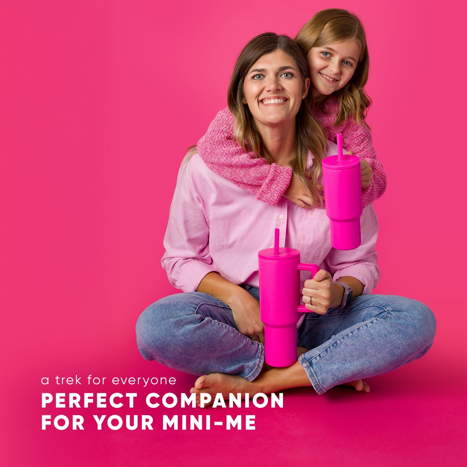 Child and adult wearing matching soft pink and mauve outfits standing against vibrant hot pink background, showcasing coordinating family look.