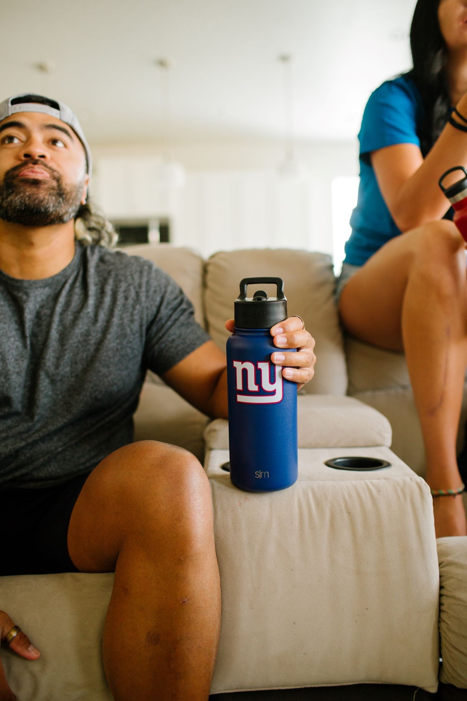 Blue water bottle on cream-colored couch next to folded tan and gray textiles, showcasing home decor styling with neutral tones and accent colors