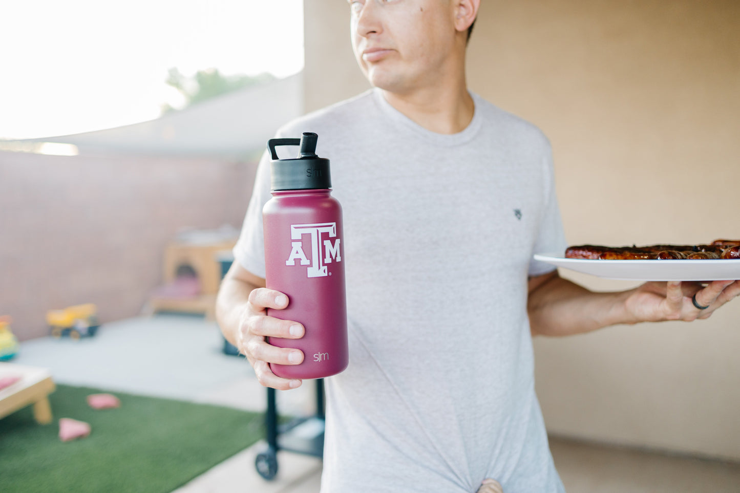 Person holding a burgundy water bottle against a soft beige and cream background