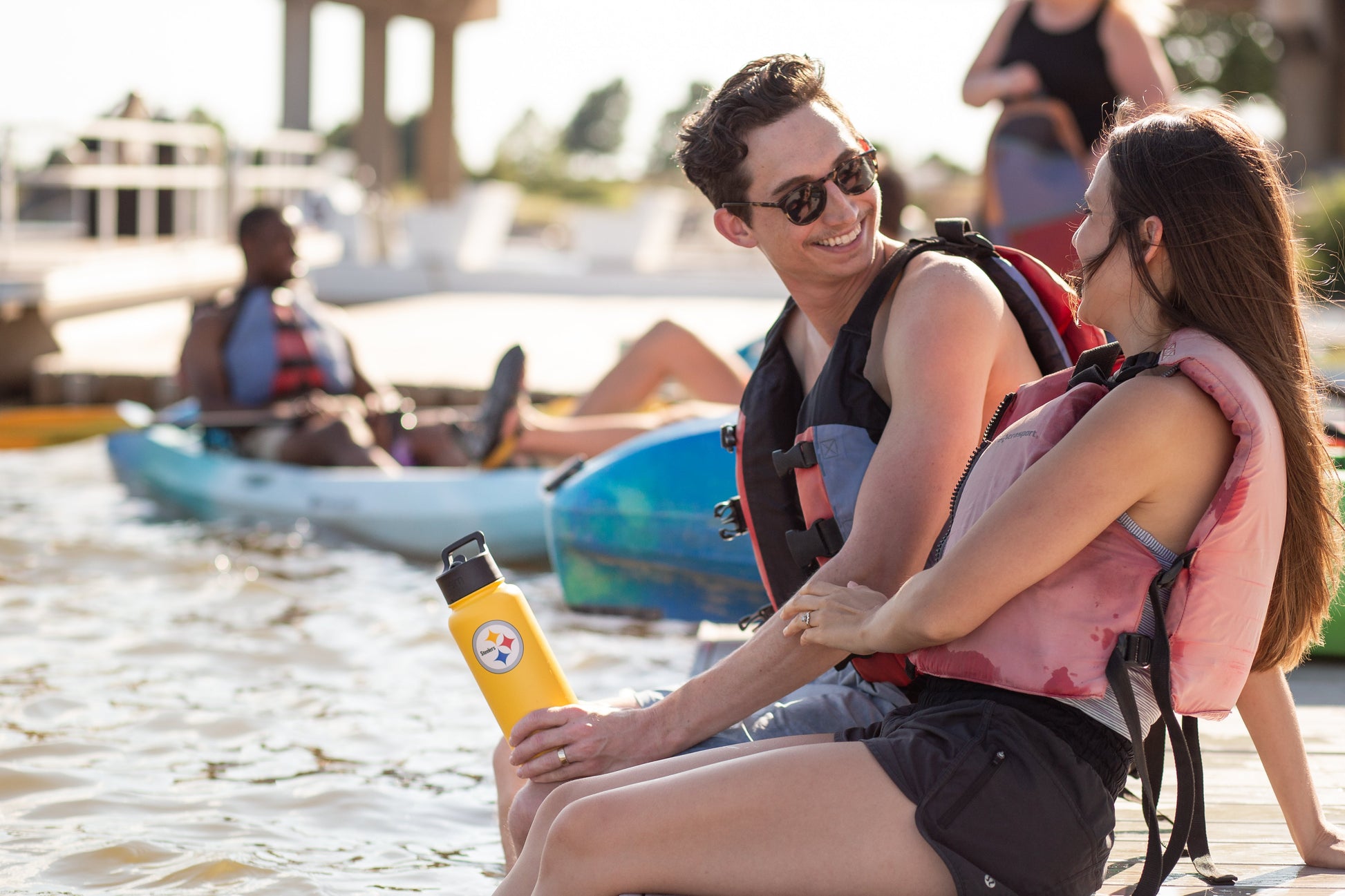 Man holding bright yellow water bottle with kayak and sky blue water in background