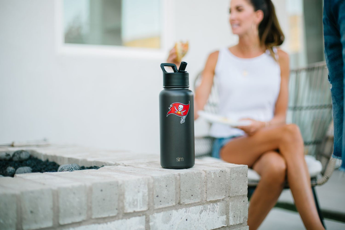 Matte black water bottle positioned on light gray concrete surface with blurred white building structures in the background