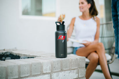 Matte black water bottle positioned on light gray concrete surface with blurred white building structures in the background