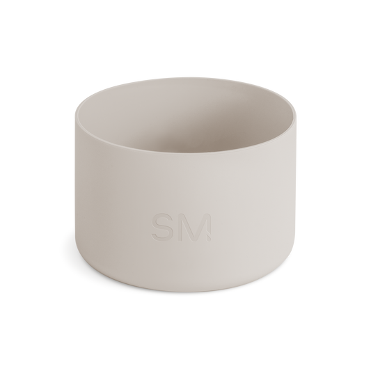 Off-white matte cylindrical boot product on pale beige background. Neutral, warm cream color palette with soft lighting.