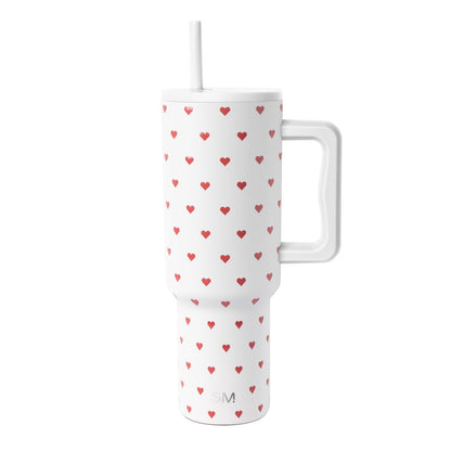 White insulated tumbler with handle and straw featuring a repeating pattern of red hearts in varying sizes.