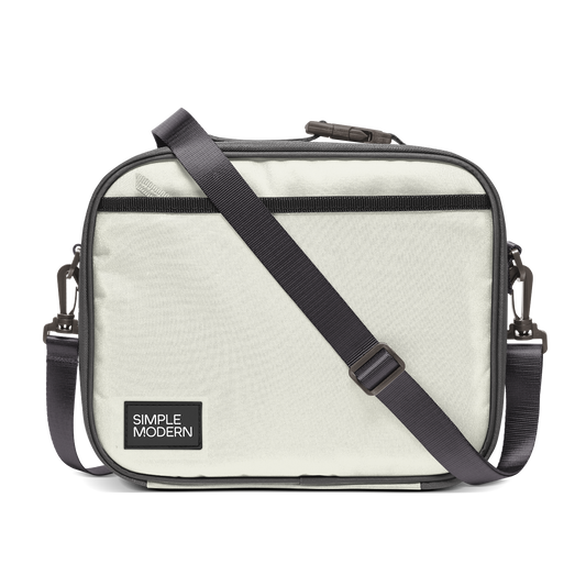 Light cream canvas tote bag with charcoal gray trim, black webbing straps, and dark hardware. Front view of structured handbag with contrasting accent details.