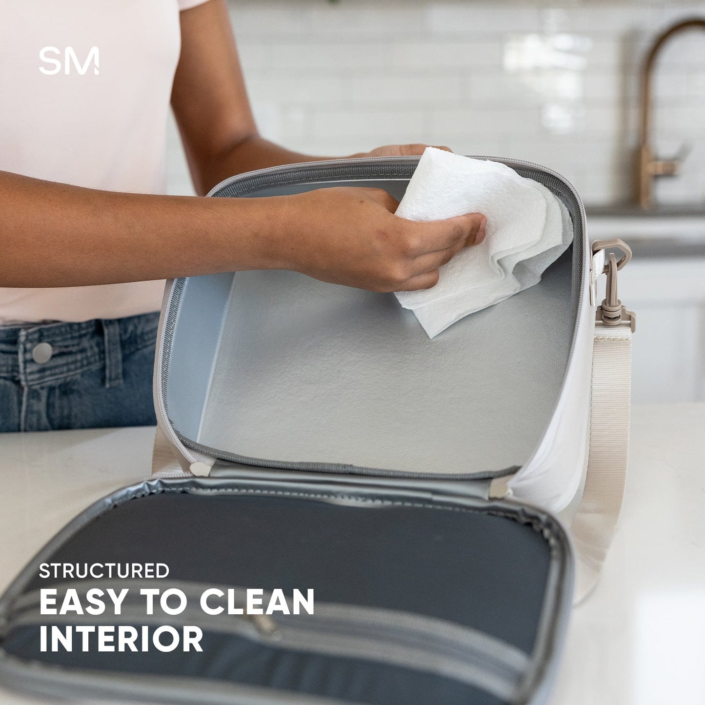 Light gray Simple Modern Hadley hardshell bag with white trim being wiped clean with a white paper towel, demonstrating easy-to-clean surface features.