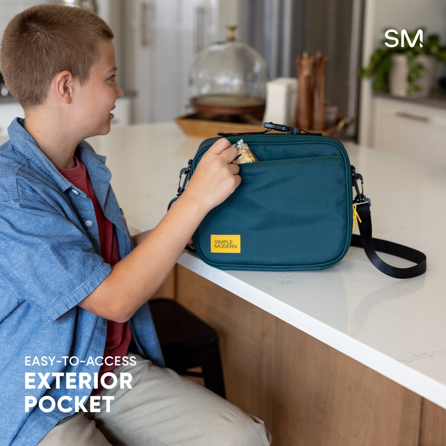 Teal hardshell case being held, showing exterior pocket detail in a warm kitchen environment with neutral tones
