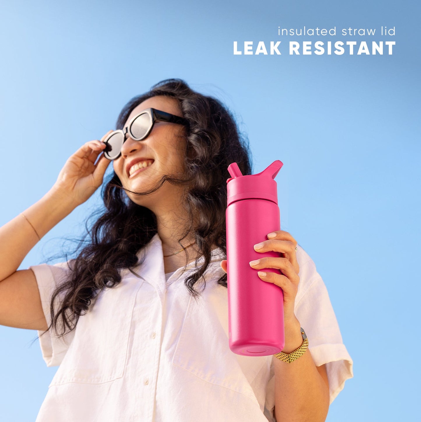 Child wearing a light pink button-up shirt holding a vibrant hot pink leak-resistant water bottle against a bright blue sky background.