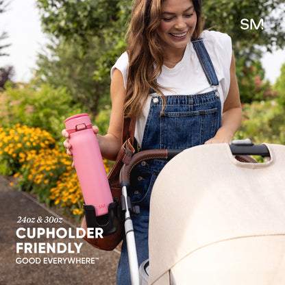Pink water bottle in cupholder of white outdoor chair with green foliage background, demonstrating Mesa Loop's cup holder-friendly design.