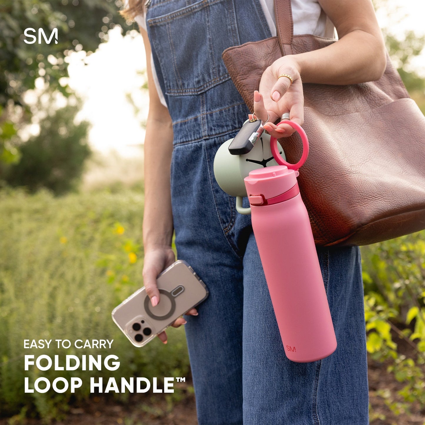 Coral pink water bottle with loop handle next to chocolate brown leather shoulder bag on medium-wash blue fabric background
