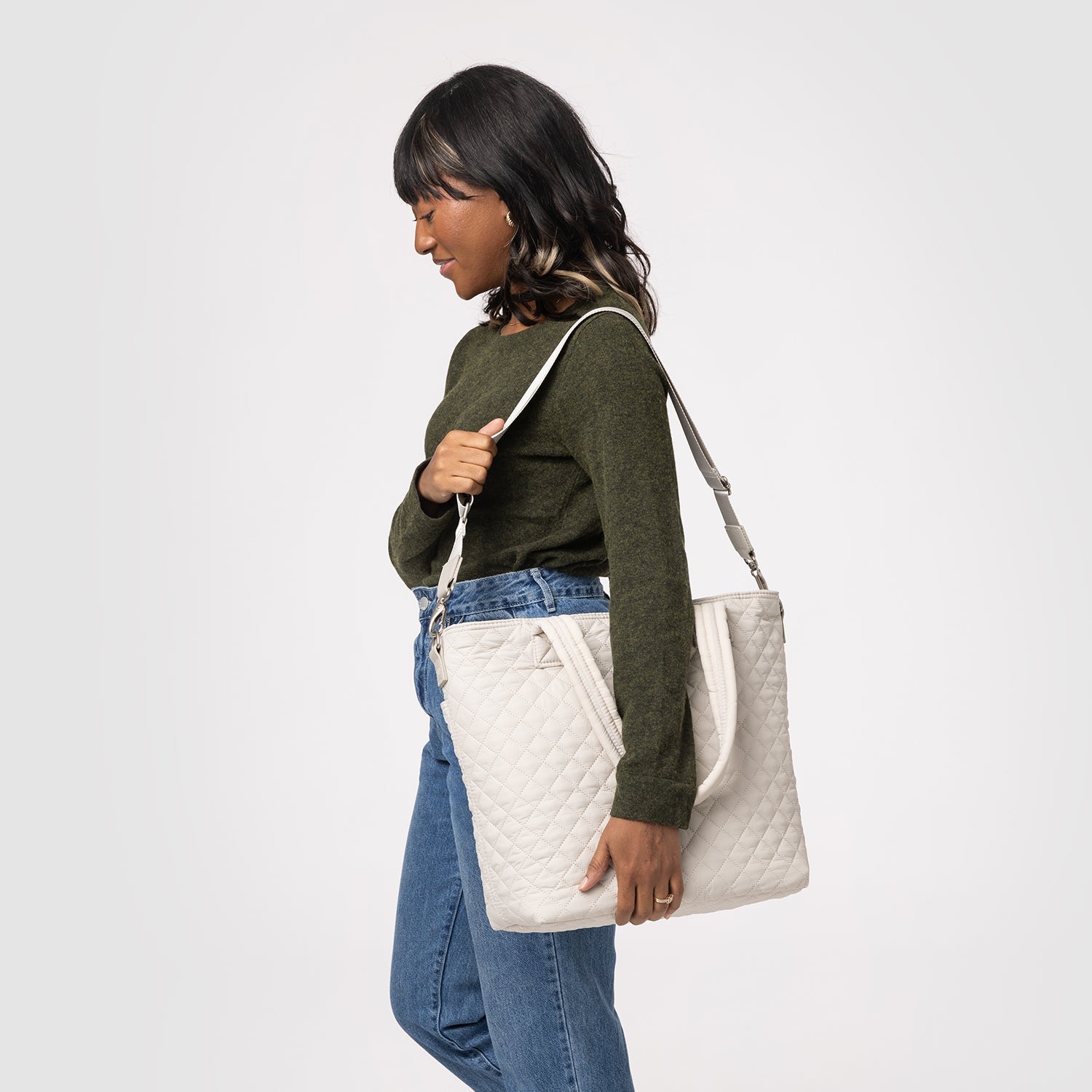 Cream quilted tote bag next to a muted olive-green long-sleeve knit top and medium-wash blue fabric, displayed against a neutral background showcasing warm and cool color tones.