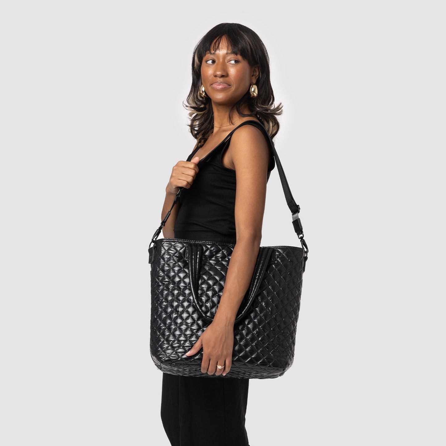 Black quilted crossbody bag with metallic gray accents displayed on model wearing sleeveless black tank top against dark background