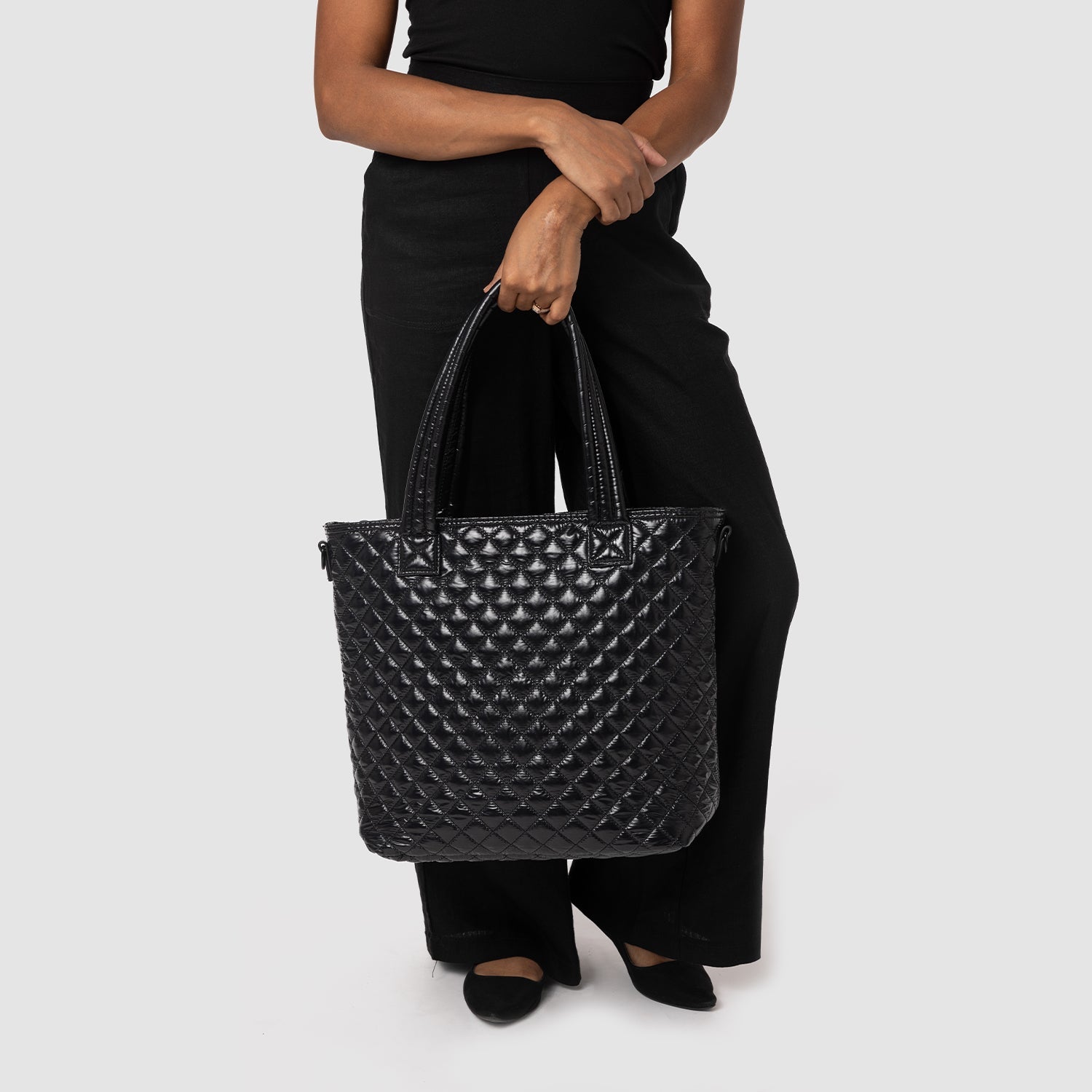 Woman wearing black short-sleeve t-shirt and distressed black pants with ripped knees, holding a quilted black tote bag
