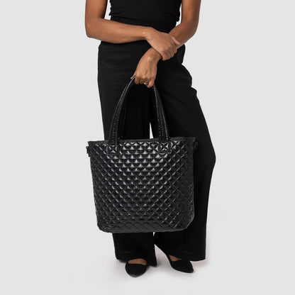 Woman wearing black short-sleeve t-shirt and distressed black pants with ripped knees, holding a quilted black tote bag