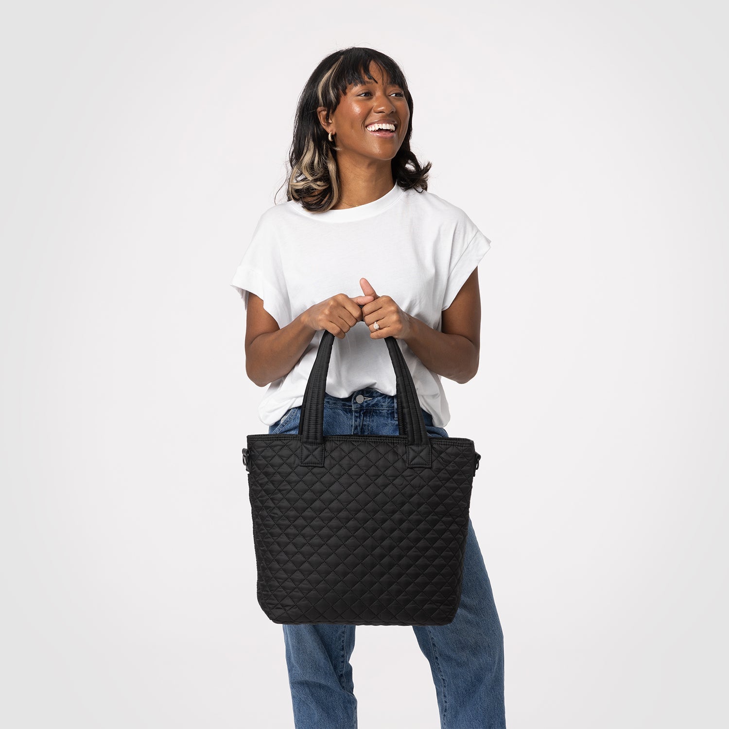 Woman wearing white t-shirt holding quilted denim blue Harper handbag against light gray background