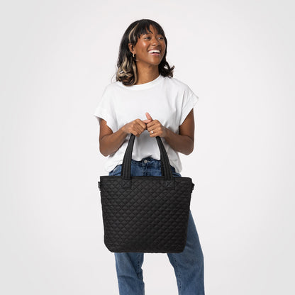 Woman wearing white t-shirt holding quilted denim blue Harper handbag against light gray background
