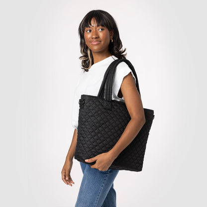 Black quilted diamond pattern tote bag displayed on model wearing white short-sleeved t-shirt against neutral background