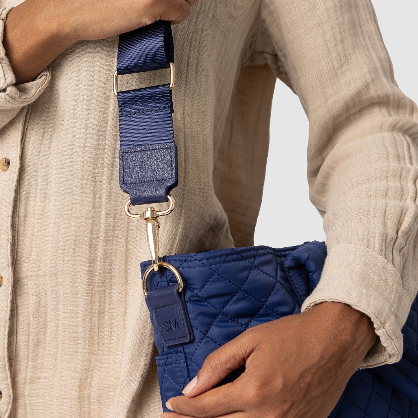 Woman wearing cream sweater and beige pants, holding quilted navy blue shoulder bag with gold accents