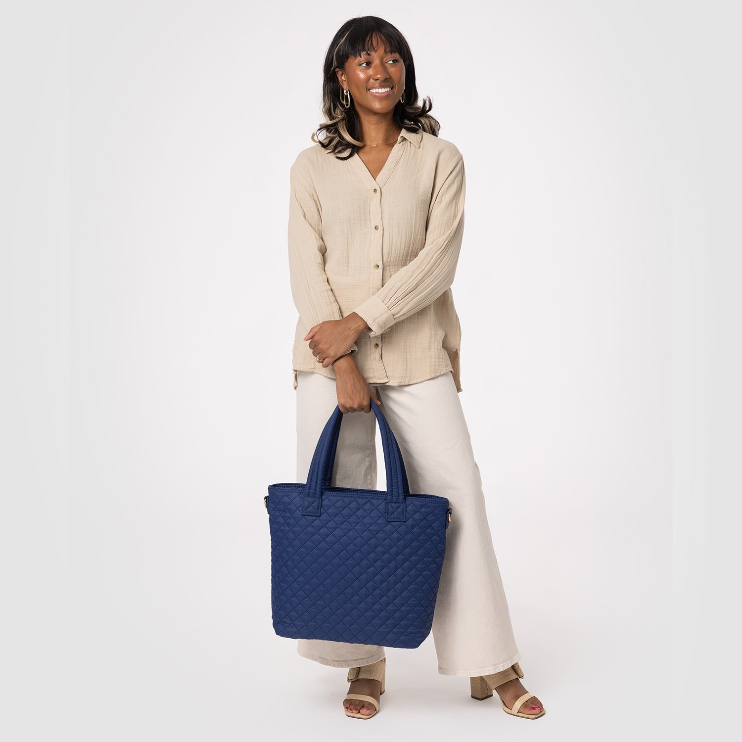 Woman wearing a cream-colored long-sleeved ribbed button-up shirt with neutral beige pants against a soft gray-white background.
