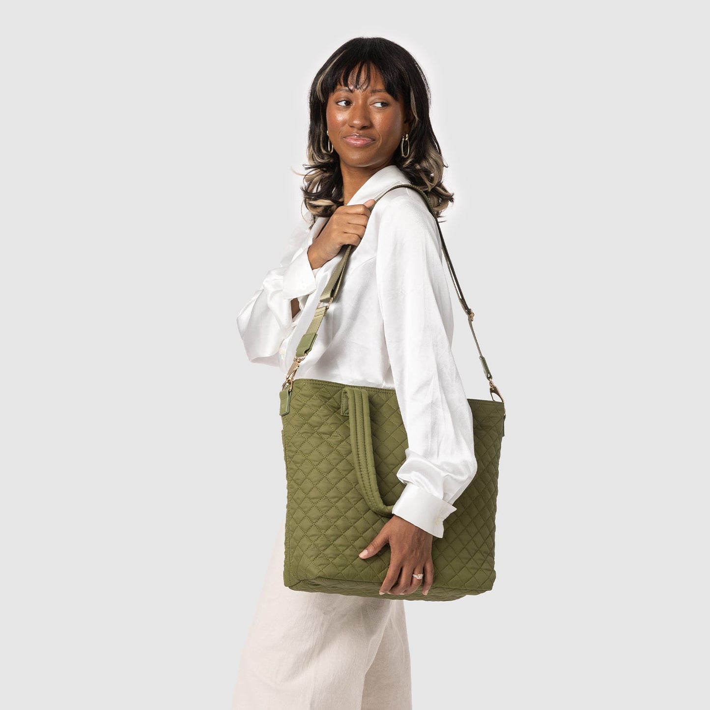 Woman wearing a crisp white button-up shirt with olive green quilted vest over pale gray background