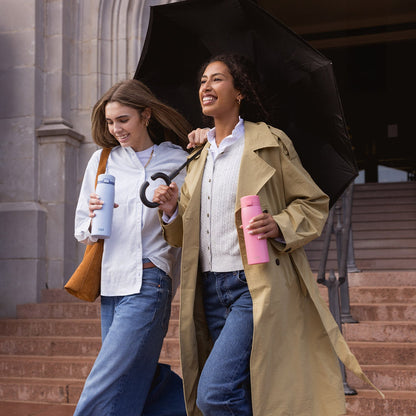 Beige and tan architectural background with two figures, one holding a soft blue water bottle, in warm earth-tone clothing