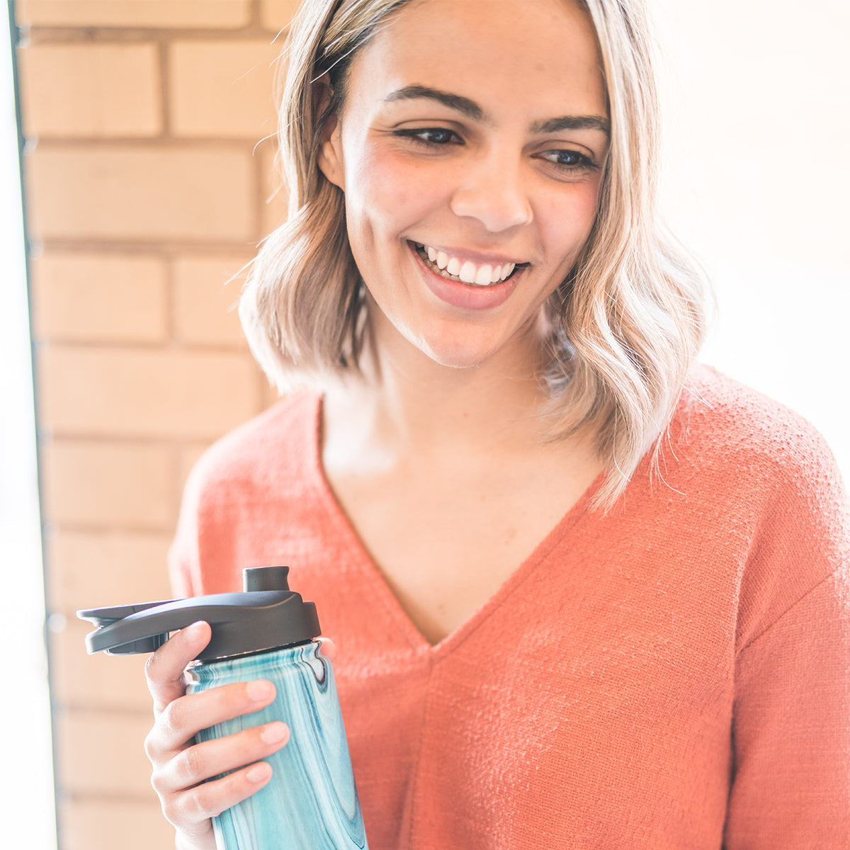 Woman wearing a coral-pink v-neck sweater and light turquoise blue garment smiling outdoors in natural daylight
