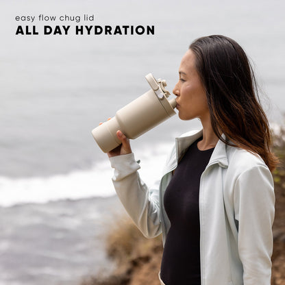 Person in cream-colored clothing holding a pale beige water bottle with a chug lid against a gray and white background.