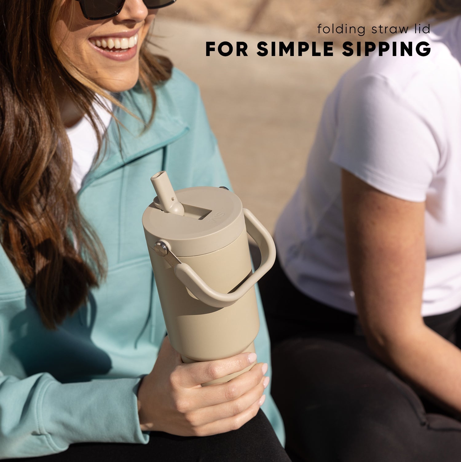 Cream-colored insulated tumbler with folding straw, held by person wearing soft blue-gray jacket in natural sunlight