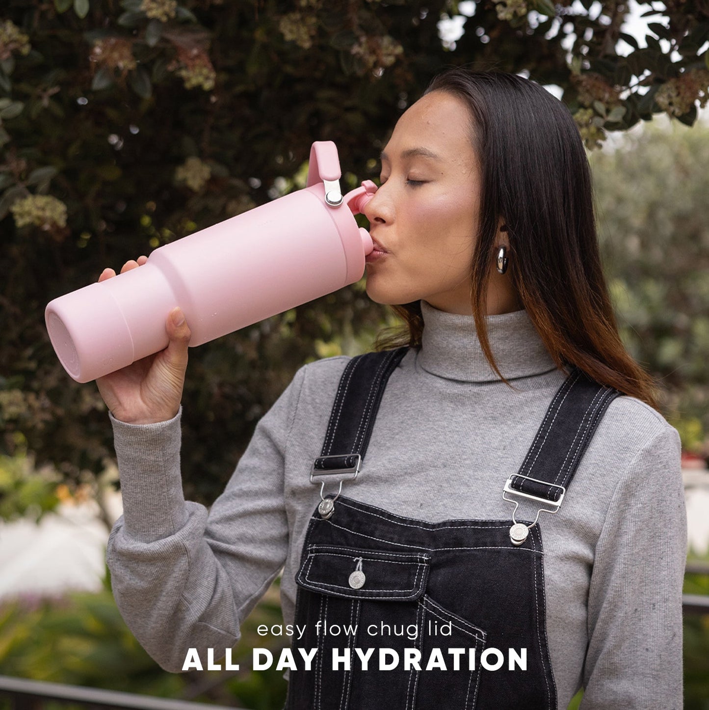 Soft pink water bottle with grip design held by person wearing gray-beige turtleneck and black denim
