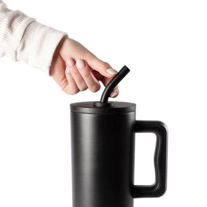 Black matte cylindrical mug with matching silicone straw held in hand against cream knit fabric background