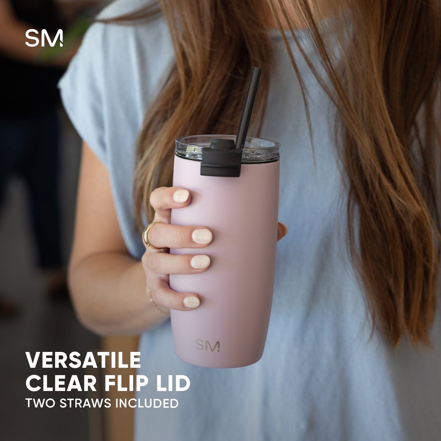 Pale pink tumbler with flip lid held by person wearing blue-gray clothing against blurred warm background