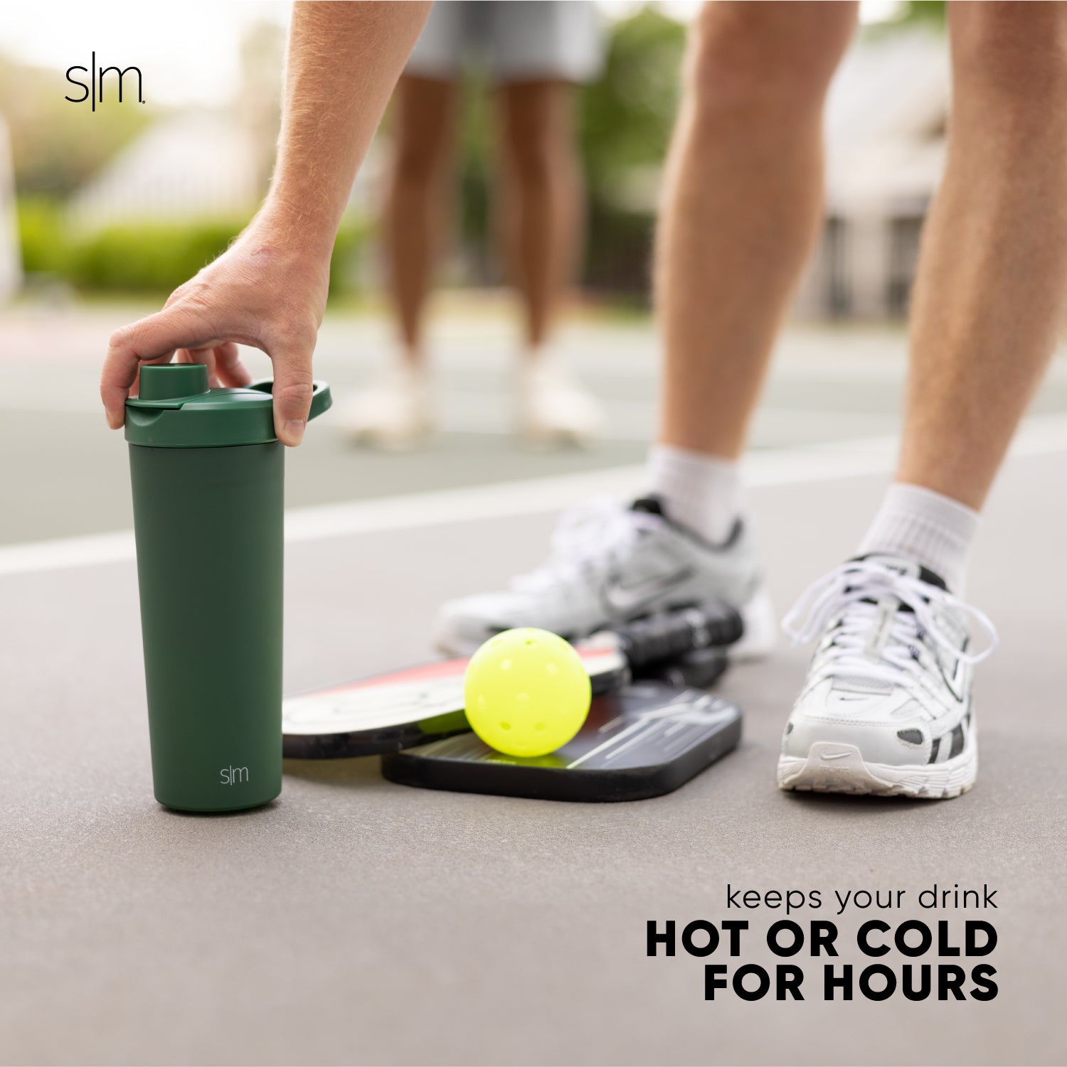 Forest green insulated tumbler next to white athletic shoes, white crew socks with black stripes, and light gray concrete pavement