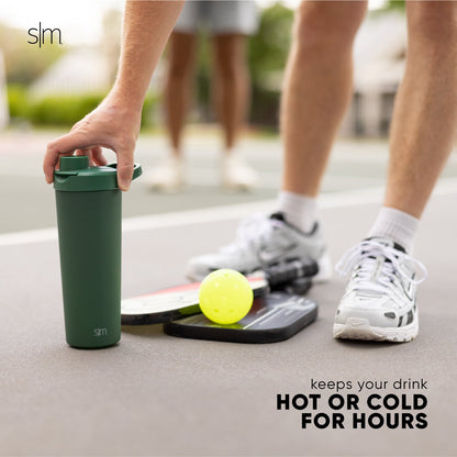 Forest green insulated tumbler next to white athletic shoes, white crew socks with black stripes, and light gray concrete pavement