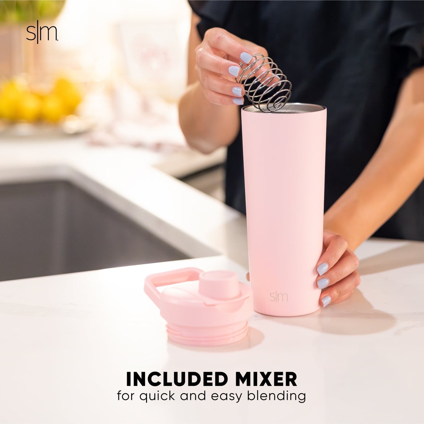 Pink ceramic mugs with white spoon on neutral kitchen countertop, person in black clothing visible, minimalist kitchen setting with soft pink and white color scheme.